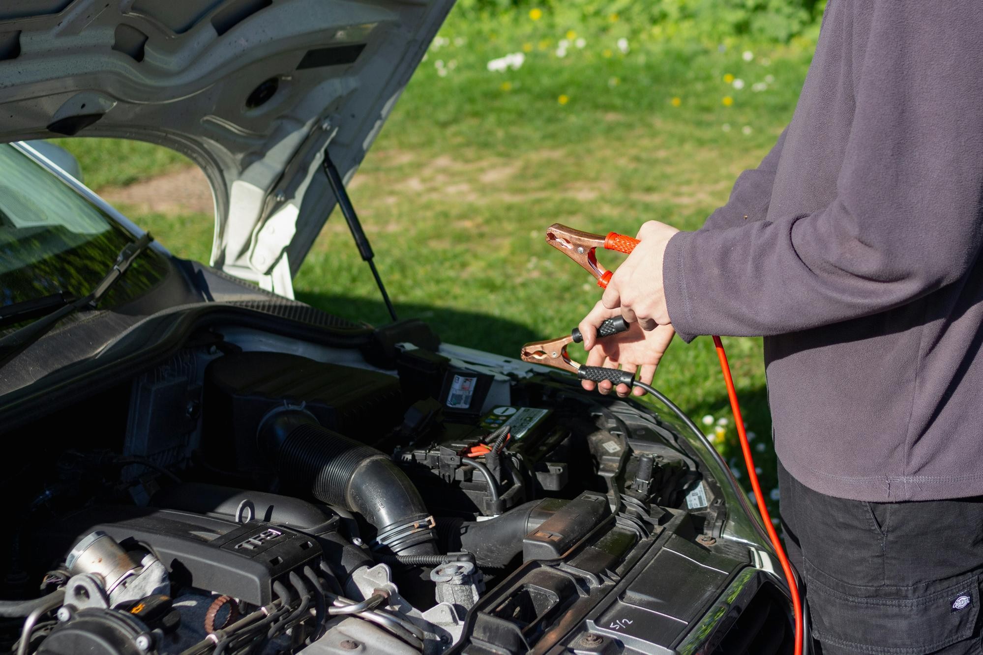 A person holding jumper cables over an open car hood