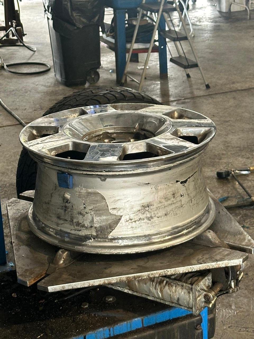 Scuffed chrome alloy wheel lying on a tire changer in a tire shop