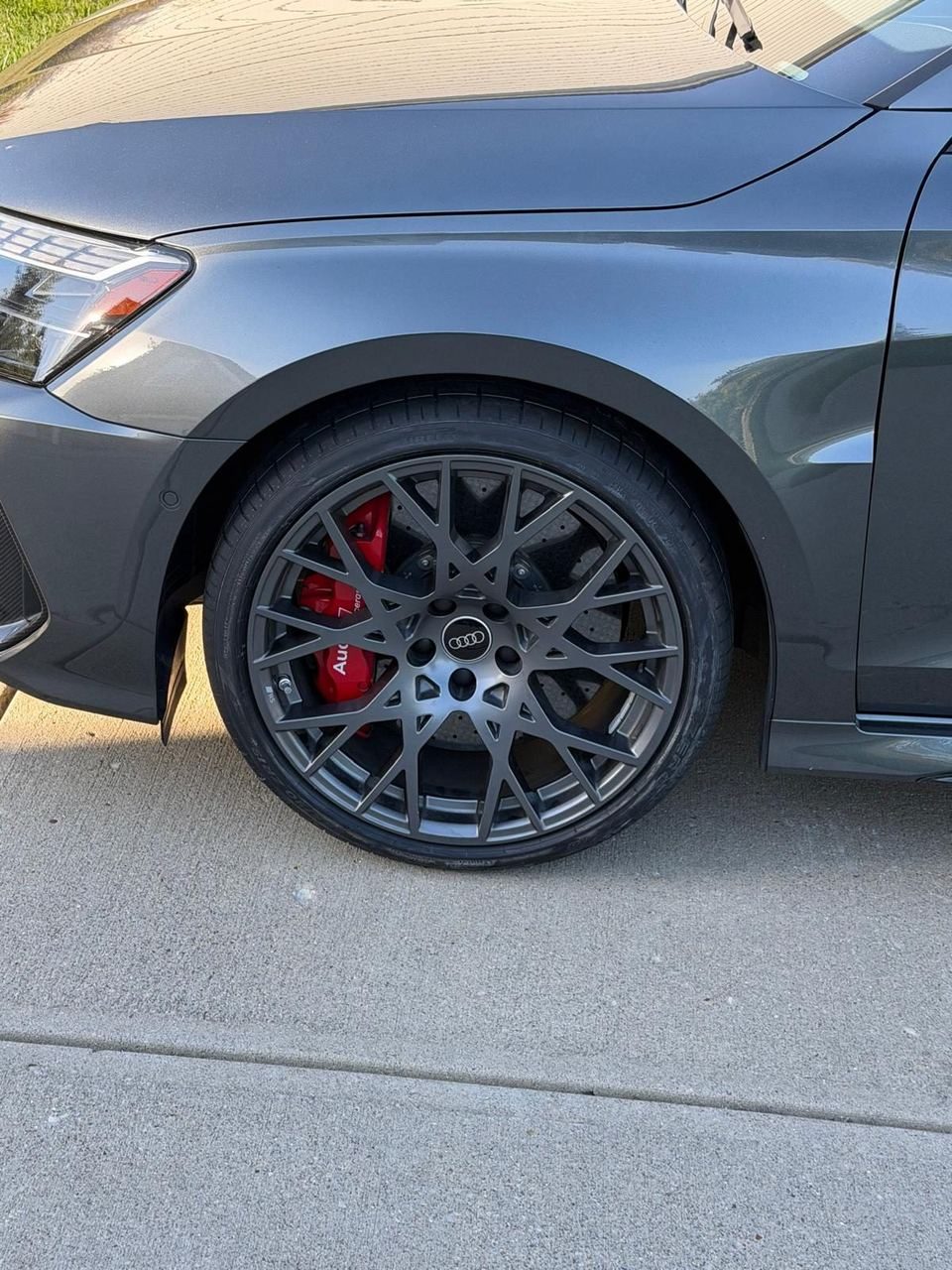 Grey Audi front wheel on a concrete driveway, a multi-spoke alloy rim held on by five lug bolts