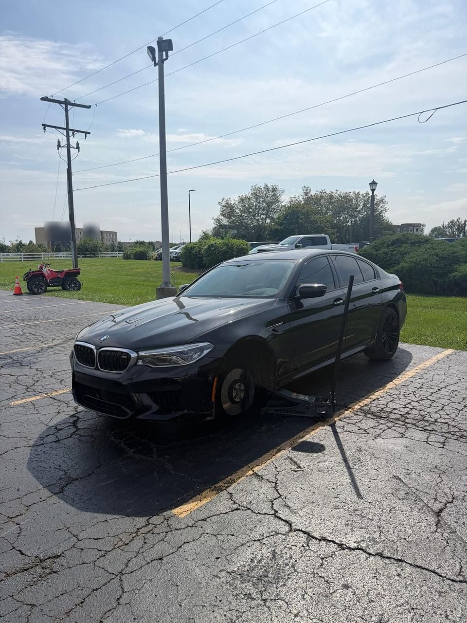 Black BMW sedan in a parking lot raised on a floor jack at the front side, with the front wheel off