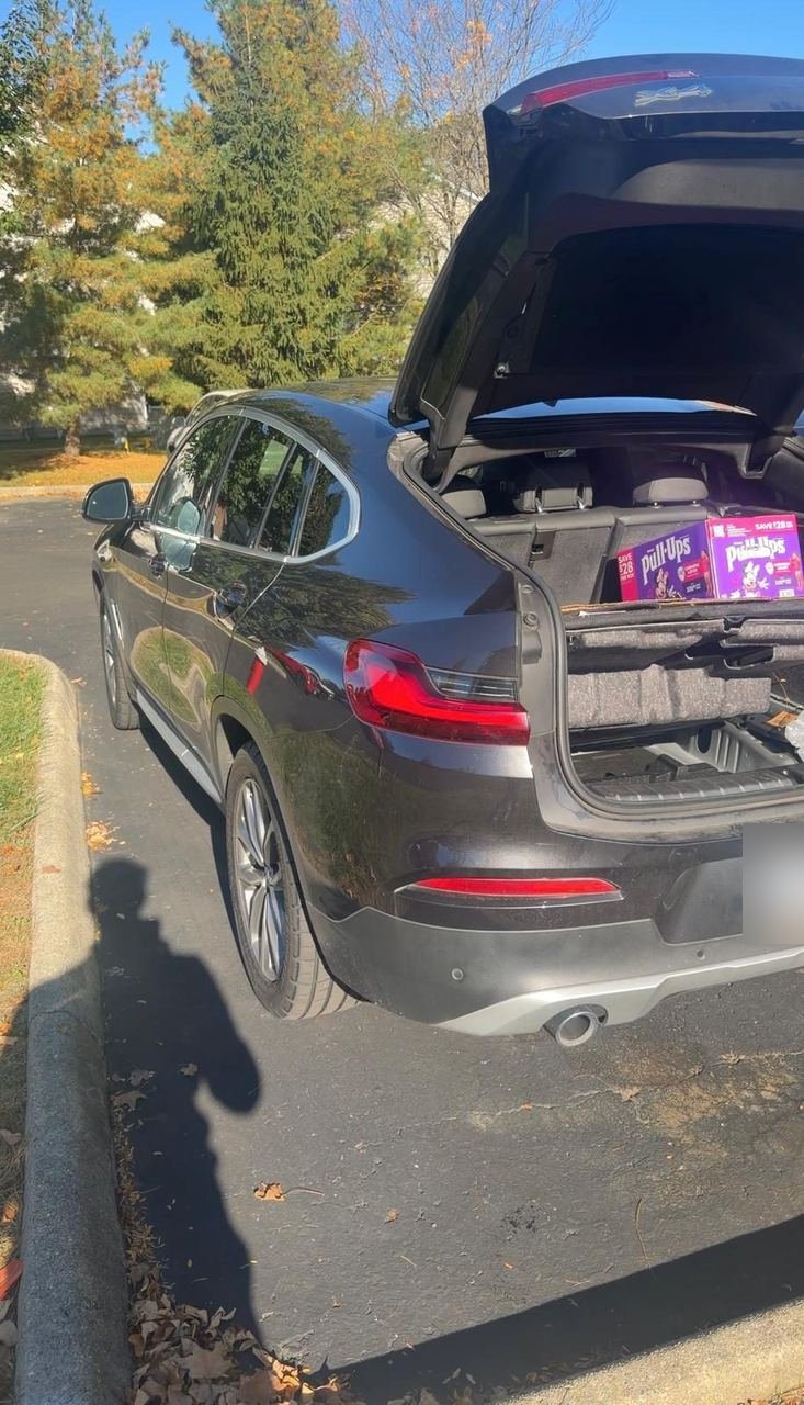 BMW X4 with its tailgate open in a parking lot during a battery replacement