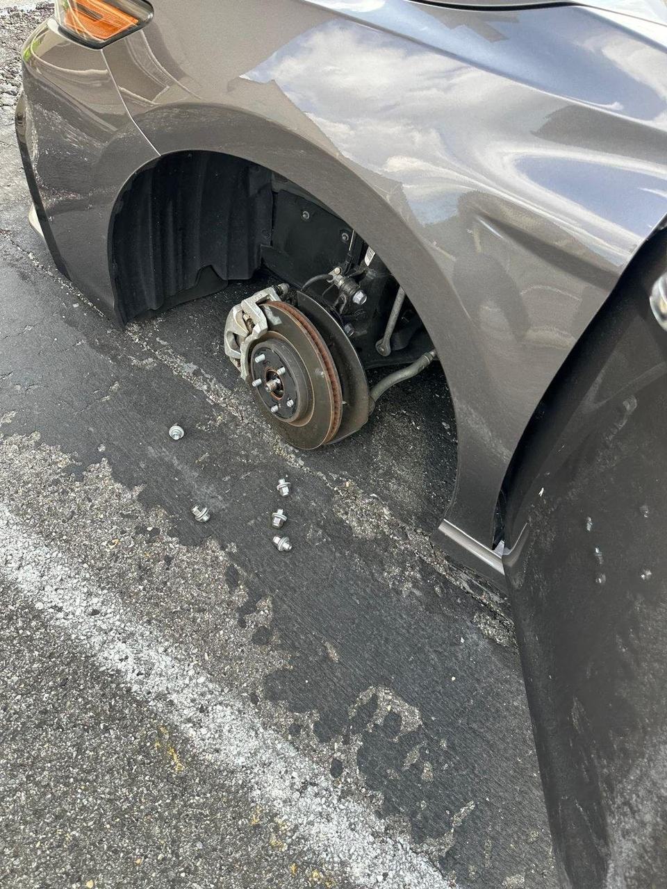 Brake rotor, caliper and wheel hub on a gray sedan with the wheel off and the lug nuts on the pavement