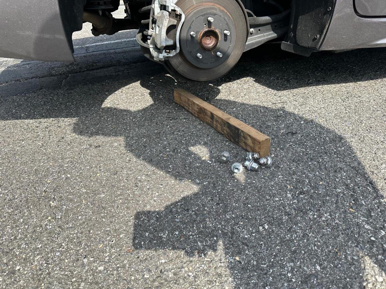 Brake rotor, caliper and hub with the wheel removed, lug nuts and a wood block on the pavement beside it