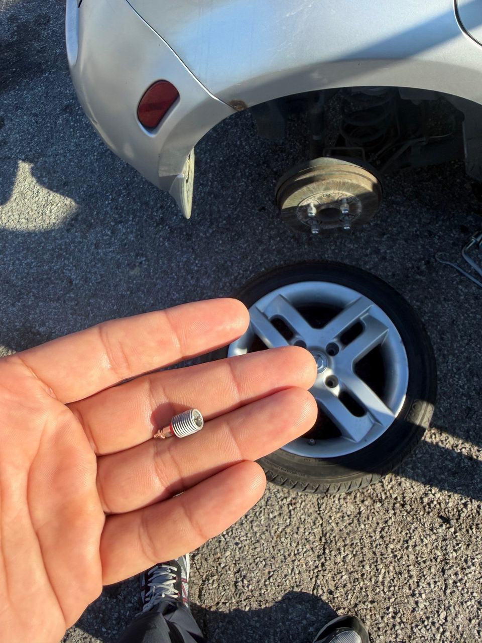 Broken tire valve held in a hand, next to the Nissan wheel taken off the car