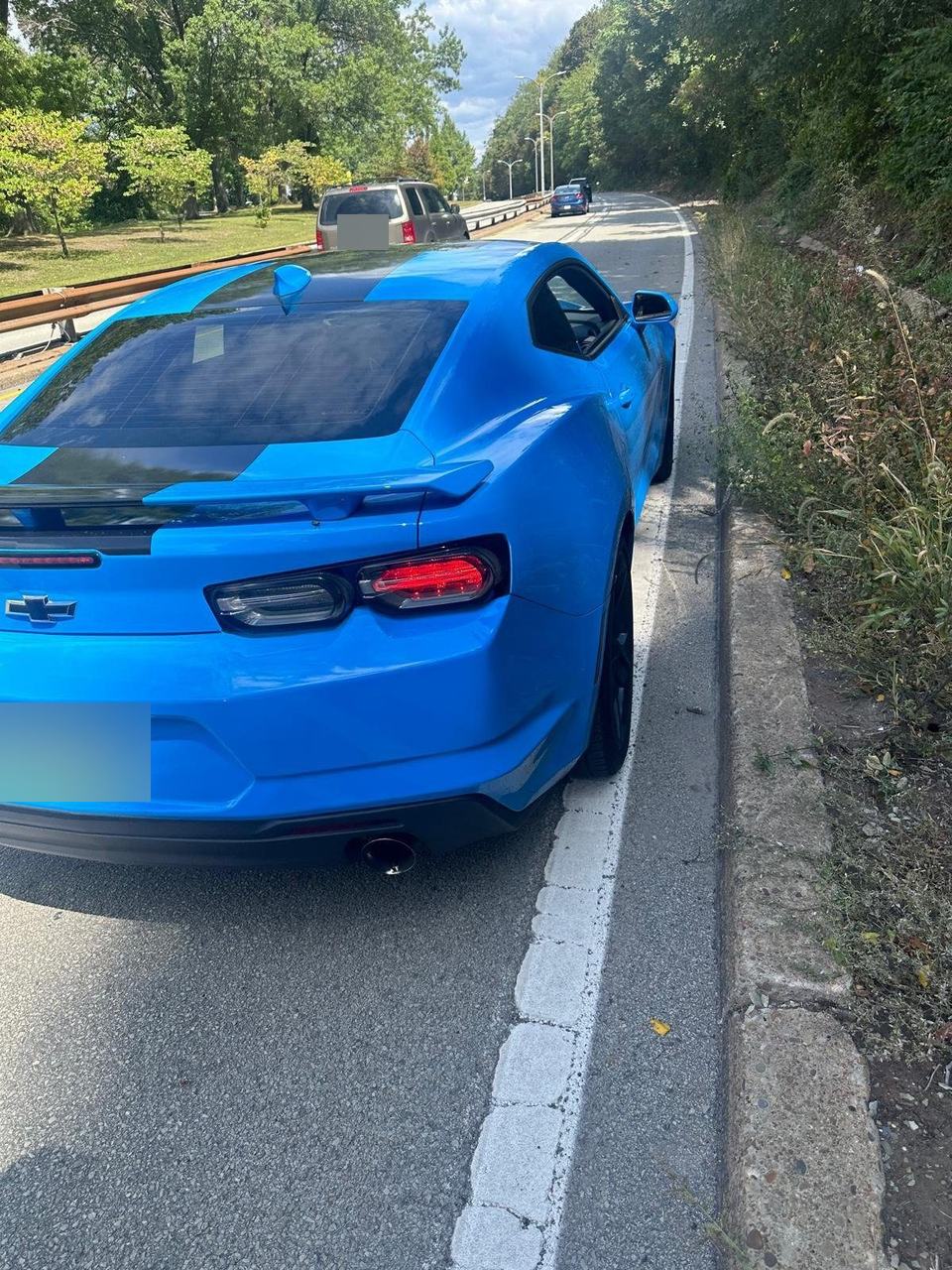 Blue sports coupe stopped at the right edge of a divided road beside a grass verge