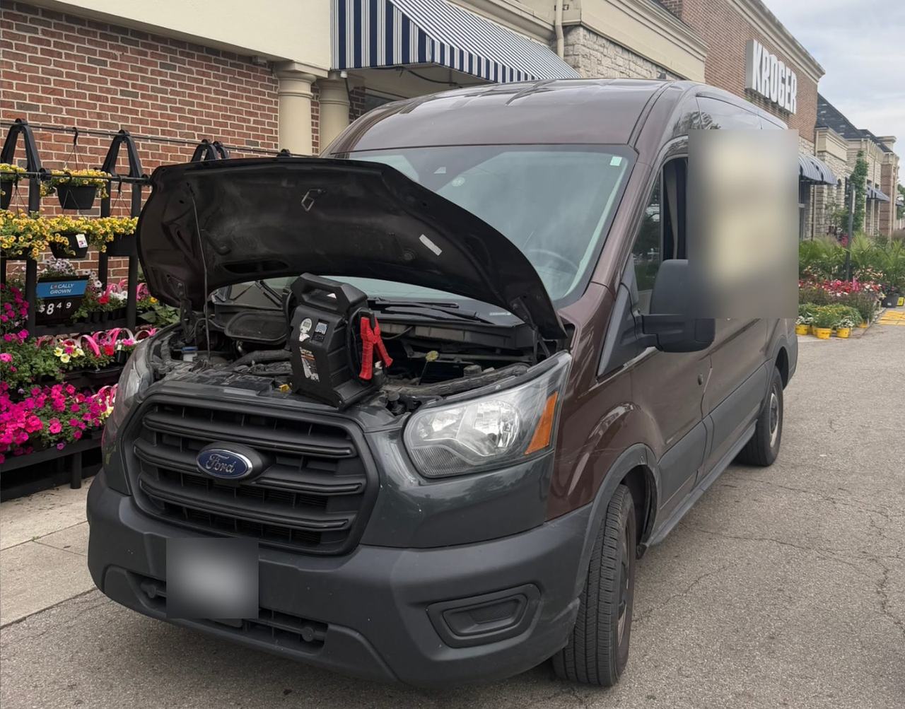 Portable jump starter on the engine of a cargo van with its hood open outside a Columbus grocery store