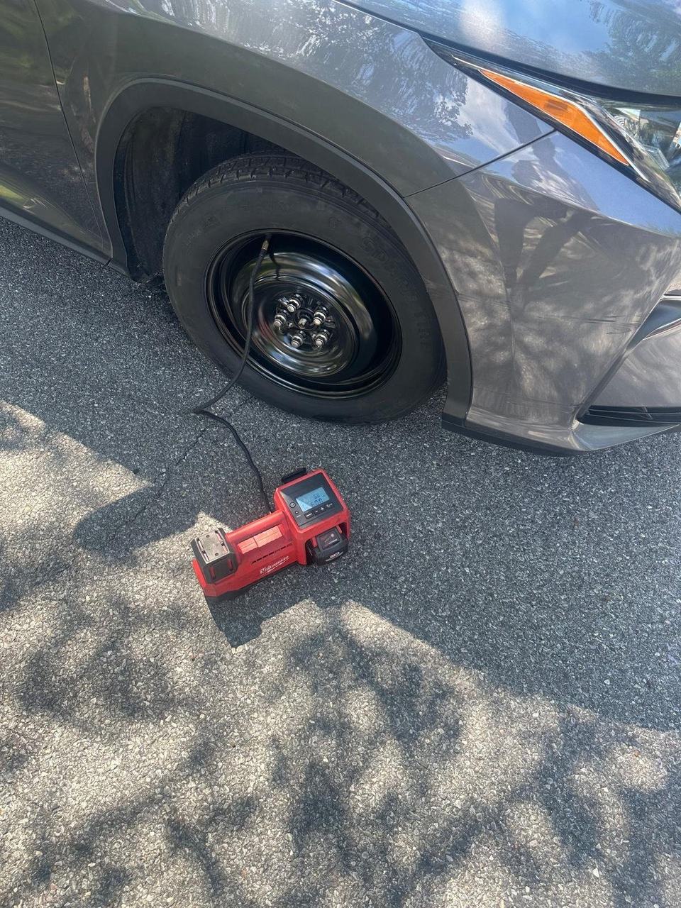 Portable air compressor on the pavement, hose connected to a spare tire on a gray SUV