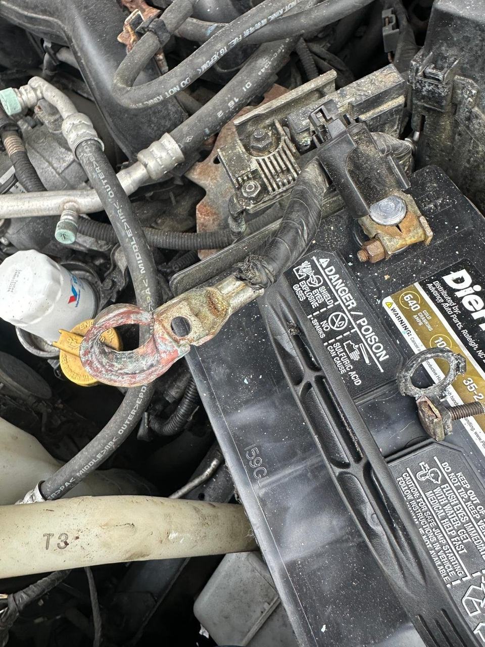 Corroded battery cable end with green and white crust beside a car battery terminal clamp