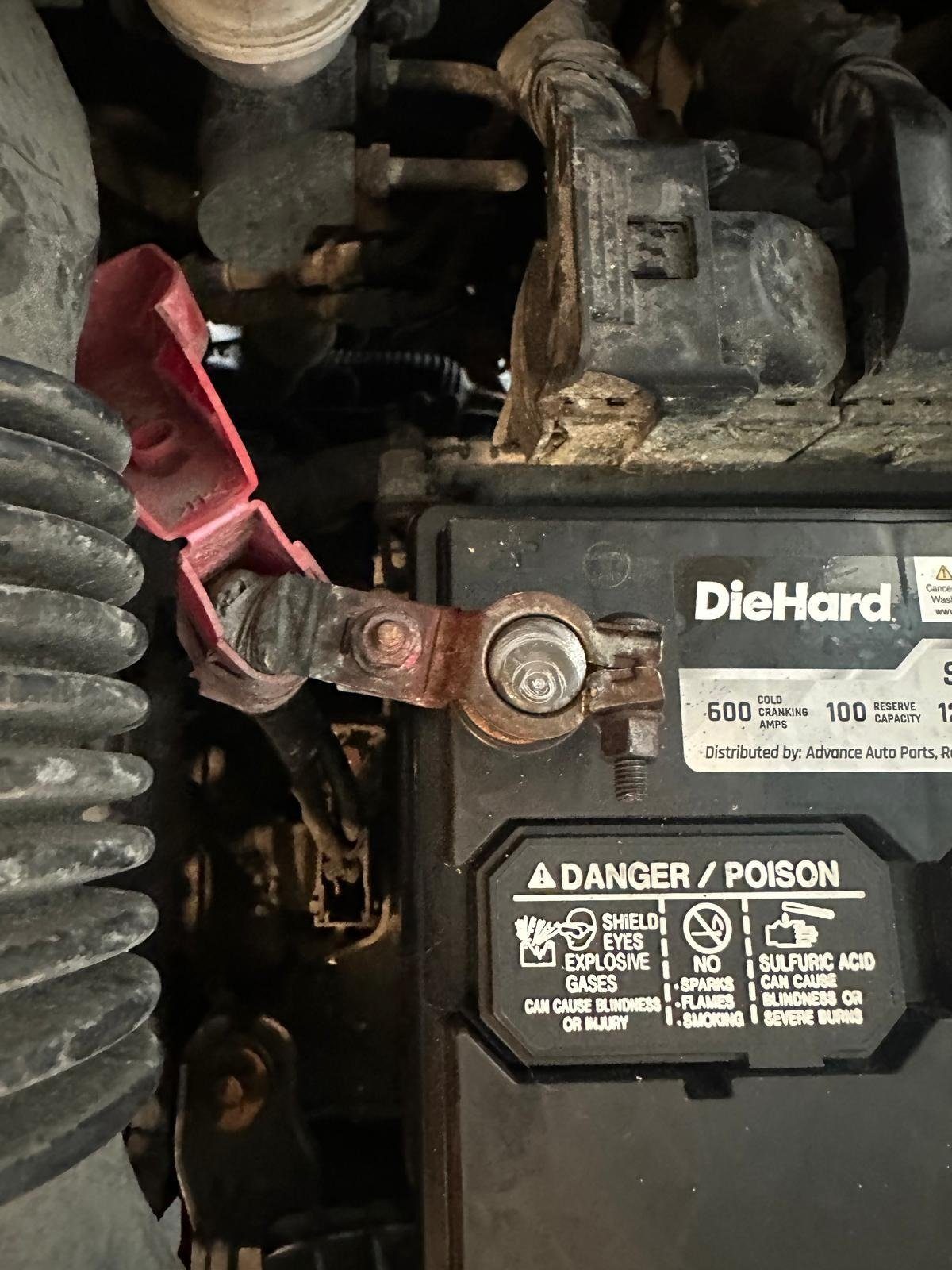 Positive battery terminal clamp with rust and corrosion on a top-post battery, red cover flipped open