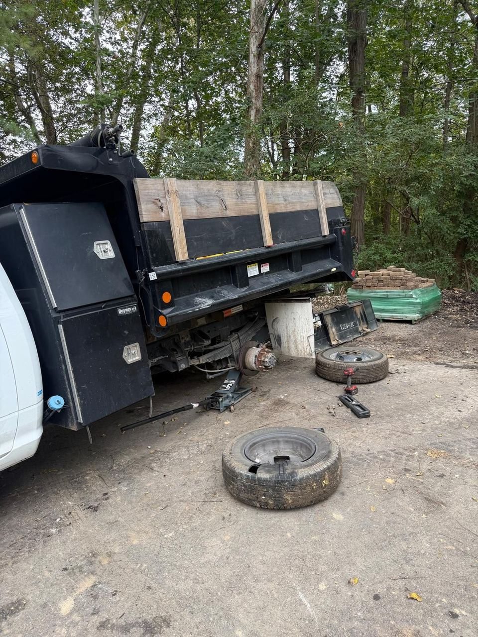Work truck on a floor jack with its rear wheels off and two removed tires lying on the ground beside it