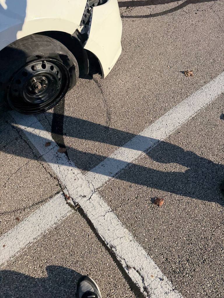 White car in a parking lot with a shredded flat tire hanging off a black steel wheel
