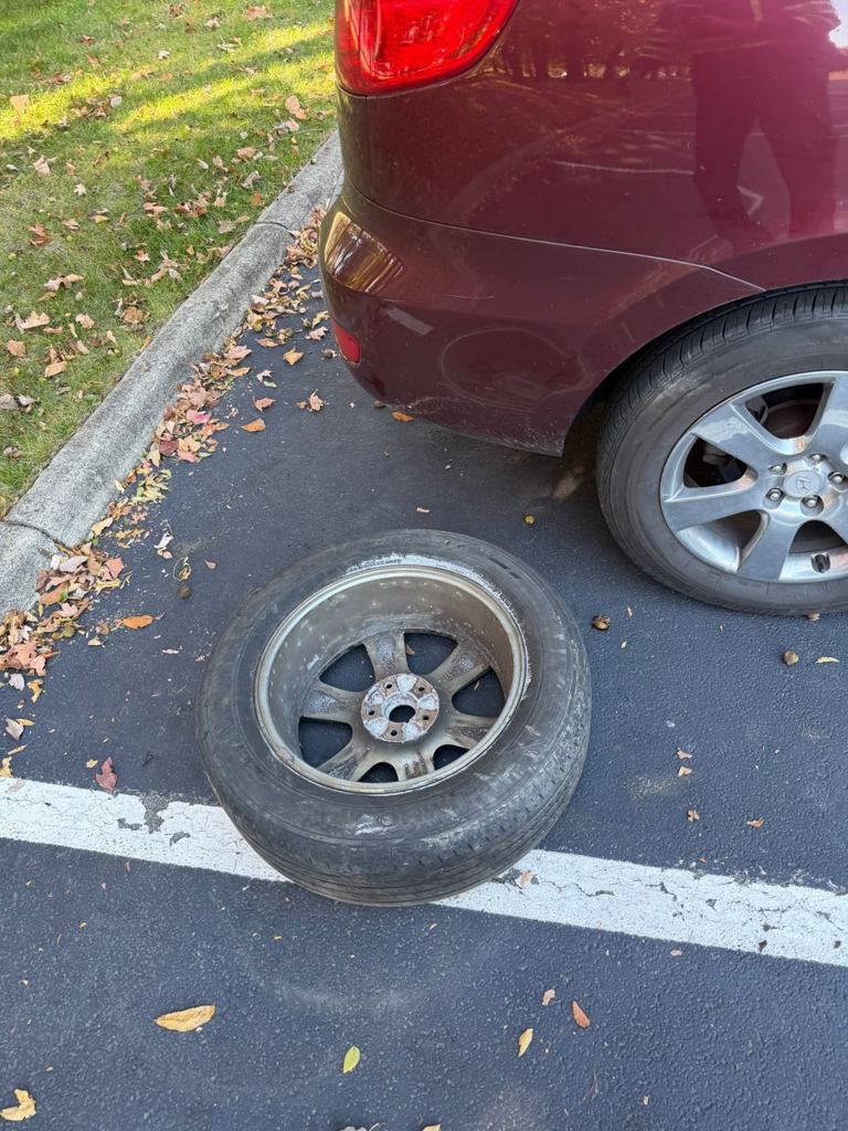 Flat tire on an alloy wheel lying on the asphalt next to the car, with the full-size spare already on