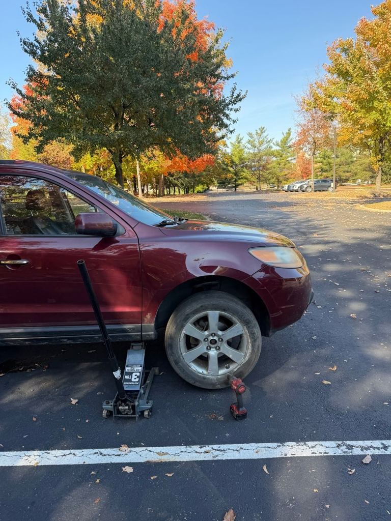 Red Hyundai Santa Fe in a parking lot with a floor jack and a cordless impact wrench beside the front wheel
