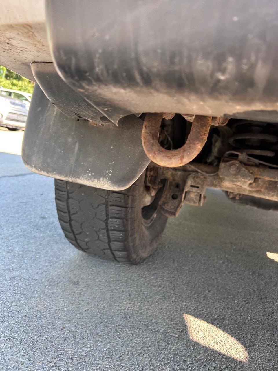 Rusty U-shaped tow hook bolted to the frame under the front of a truck, next to the front tire