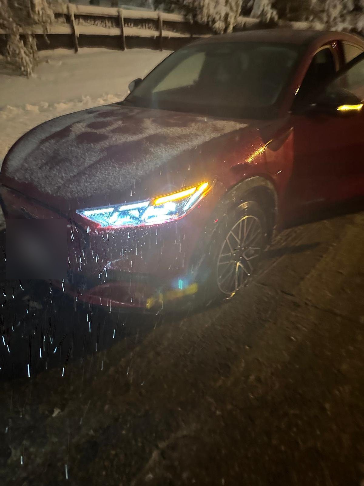 Red crossover with frost on the hood at night, headlights on, snow along the roadside