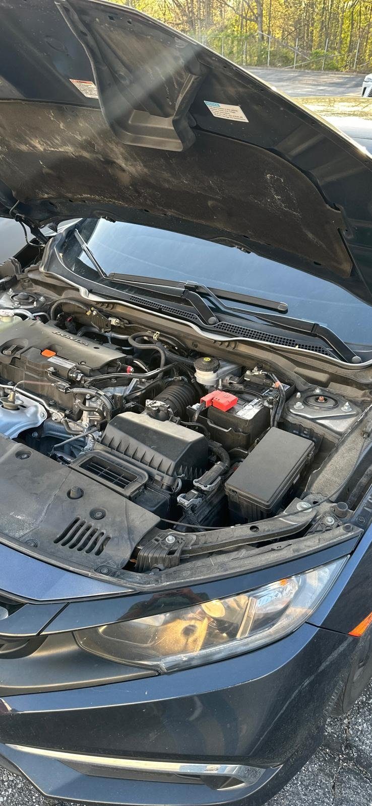 Honda sedan in a parking lot with the hood open, engine and battery visible