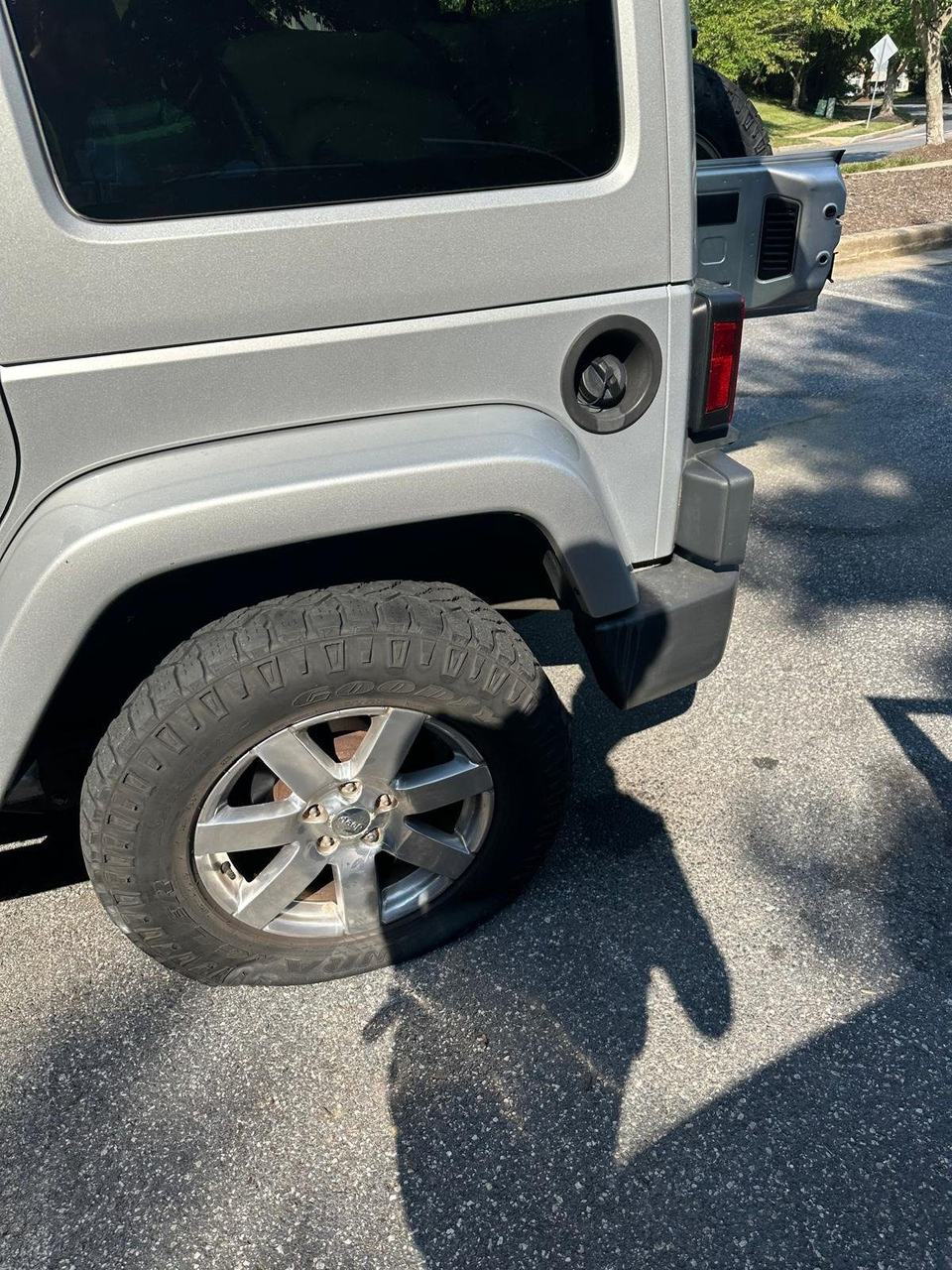 Silver Jeep Wrangler with a flat rear tire in a parking lot
