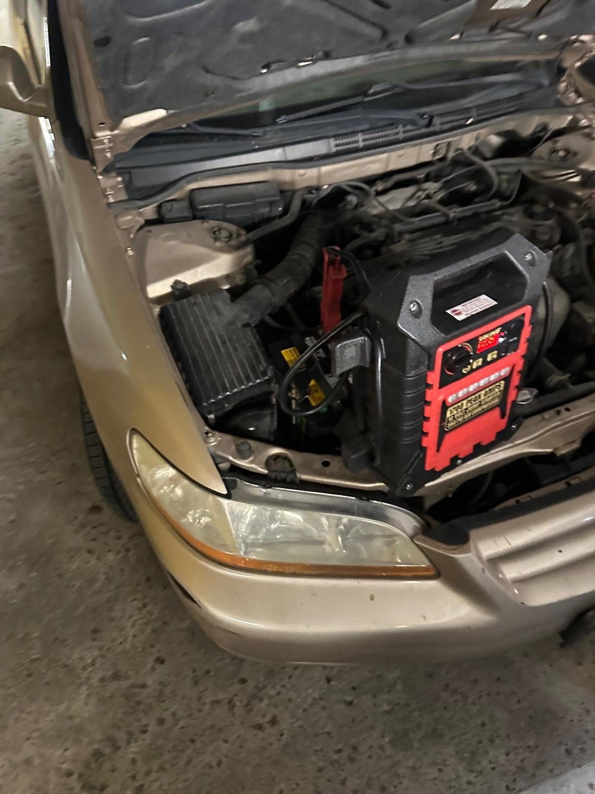 Jump pack connected to the battery of a gold sedan with the hood open in a parking garage