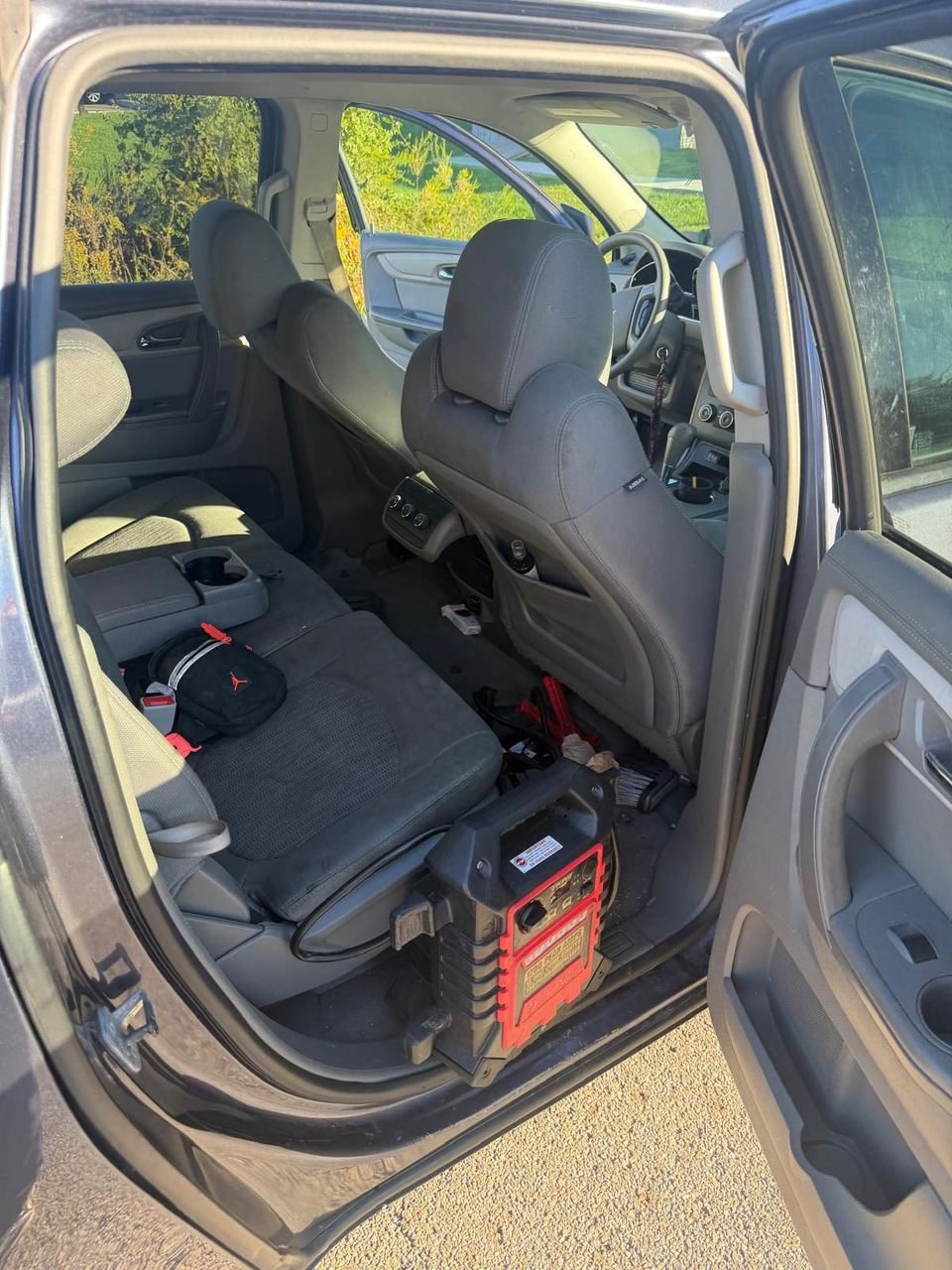 Red portable jump pack on the floor behind the front seat of an SUV with its rear door open