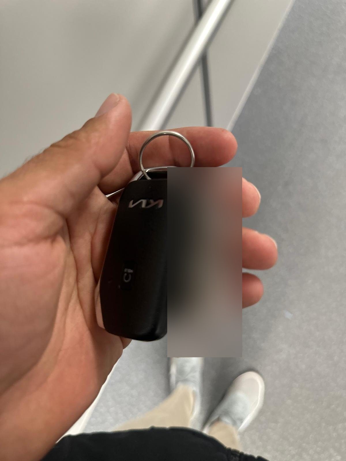 Hand holding a black Kia smart key fob on a key ring with a tag attached