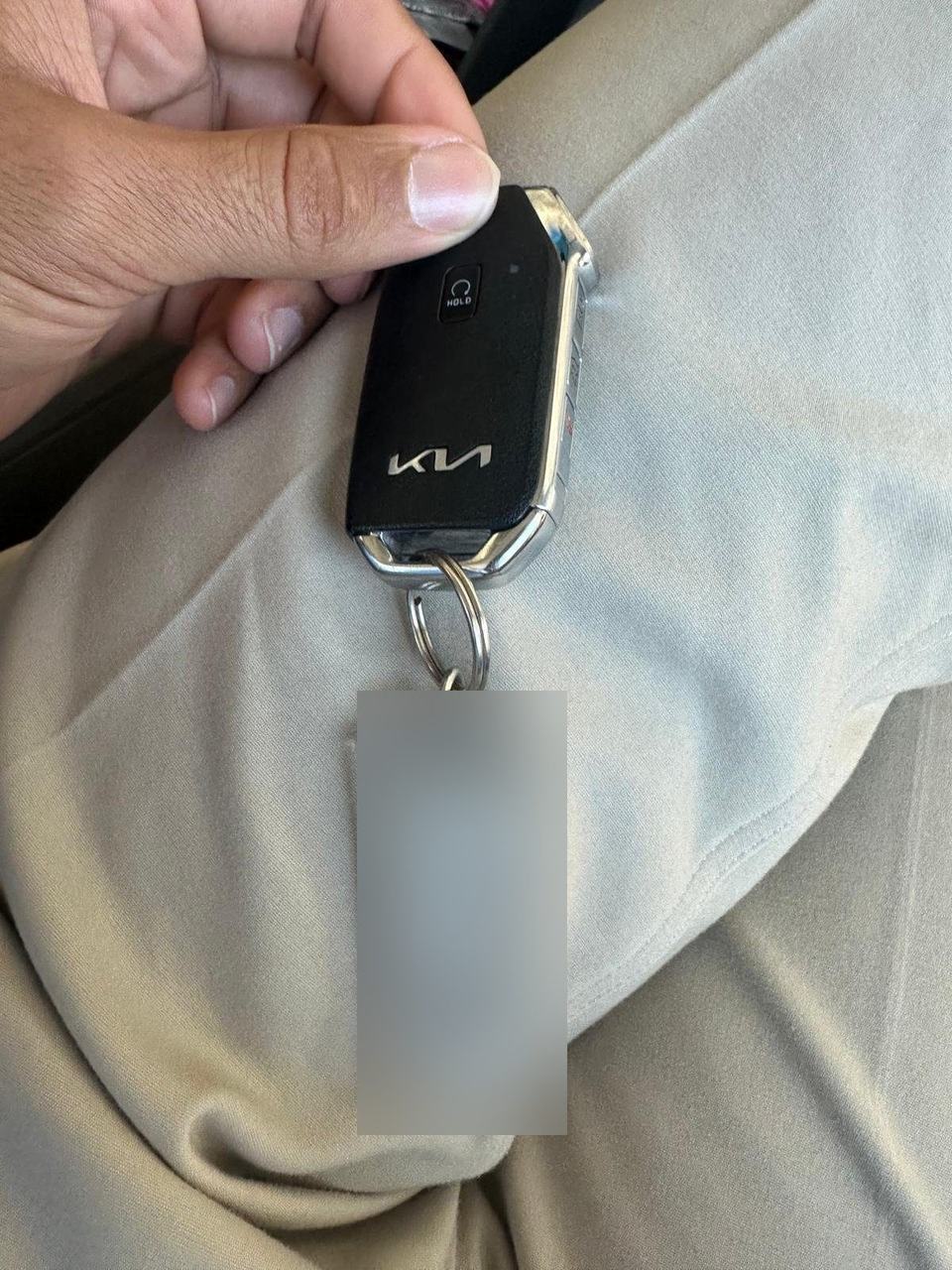 Kia smart key fob with a remote start button and a key tag on the ring, held over a car seat
