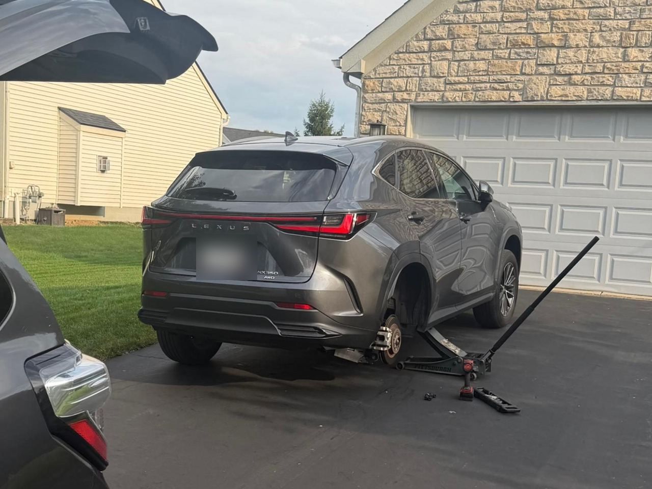 Lexus SUV raised on a jack with a rear wheel removed in a home driveway