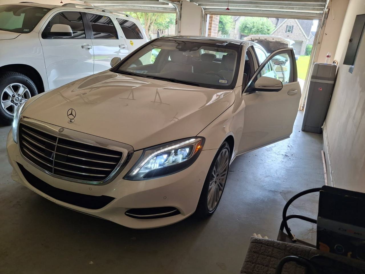 White Mercedes S-Class parked in a home garage with the driver's door open during a battery service call
