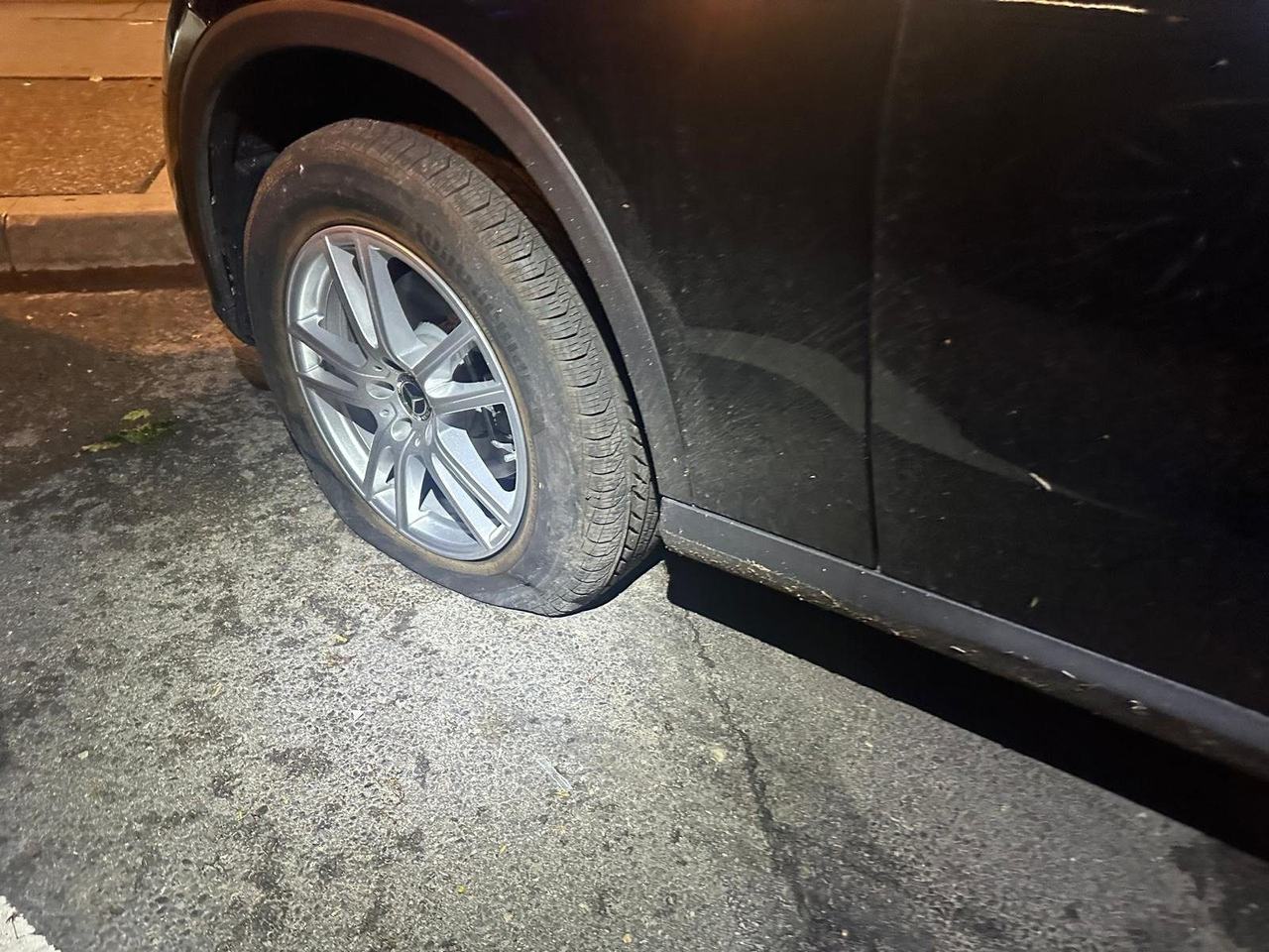 Black Mercedes SUV with a flat front tire parked at a curb at night