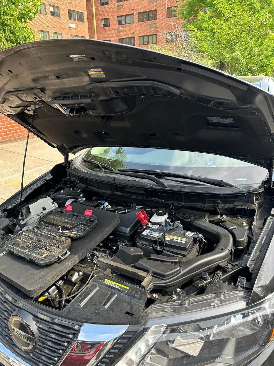 Nissan SUV with the hood open and a socket set laid on a foam mat beside the battery