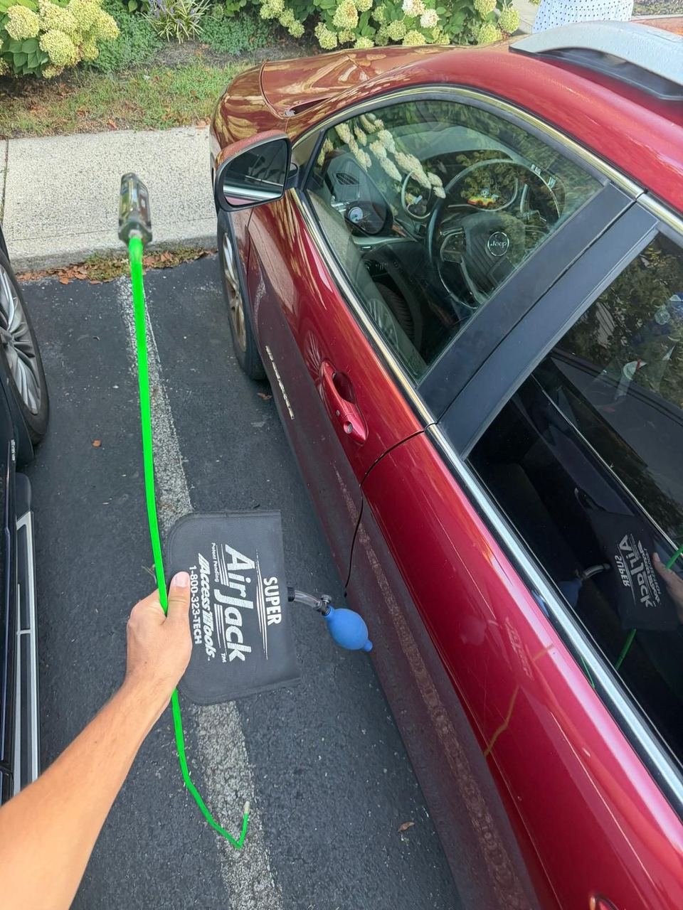 Technician using an air wedge and long-reach tool to open a locked red Nissan in a parking lot