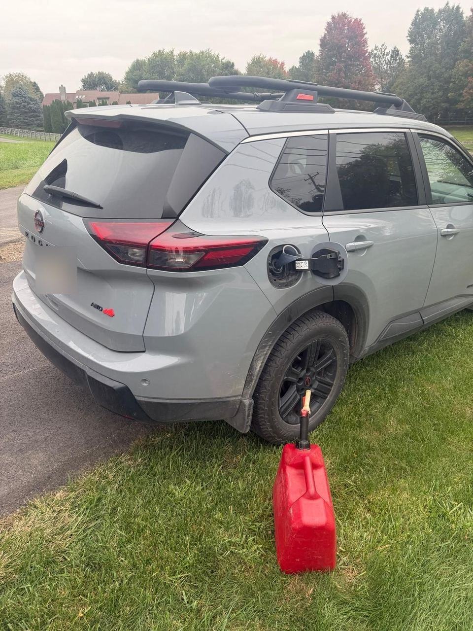 Red gas can feeding fuel into a grey Nissan Rogue parked on the grass by the road