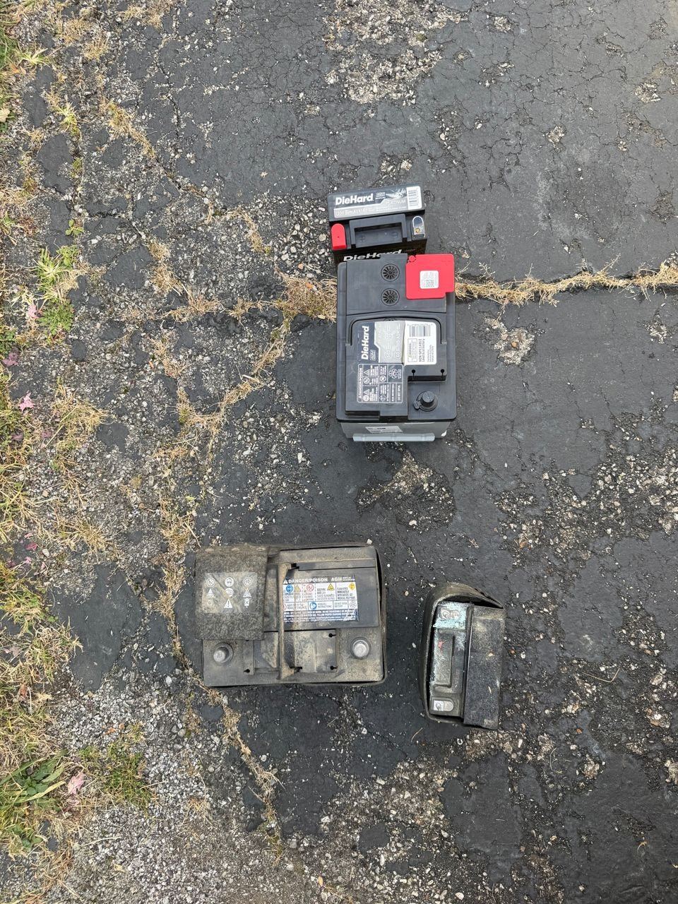 Two new DieHard batteries at the top and the two old, dirty batteries below them on an asphalt driveway