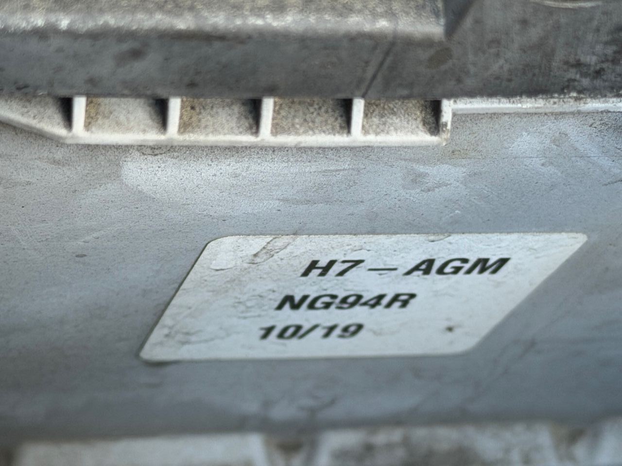 Close-up of the sticker on an old car battery reading H7-AGM, NG94R and 10/19