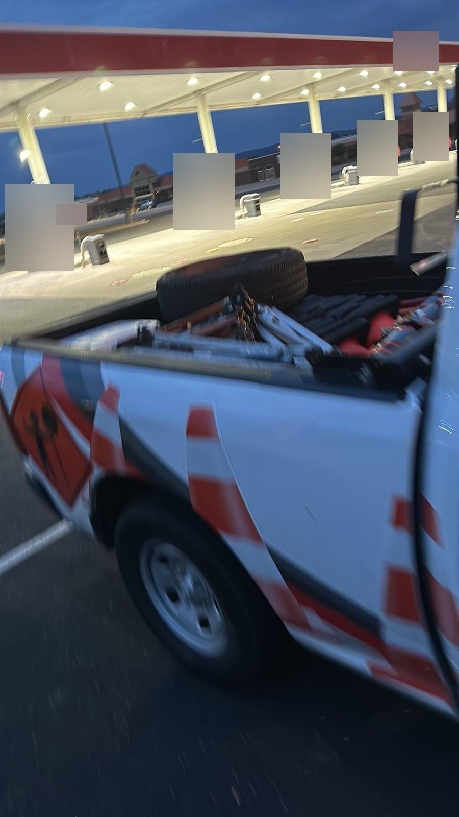 White pickup with traffic cone graphics parked at a gas station under a lit canopy at dusk