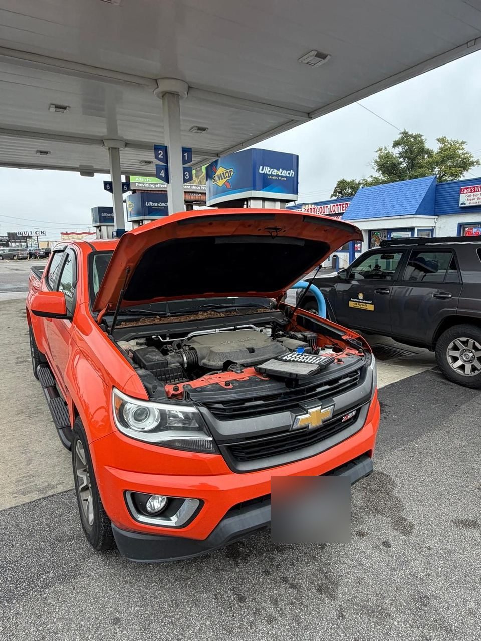 Orange Chevrolet pickup with the hood open at a fuel station, Roadmate's grey service truck parked alongside