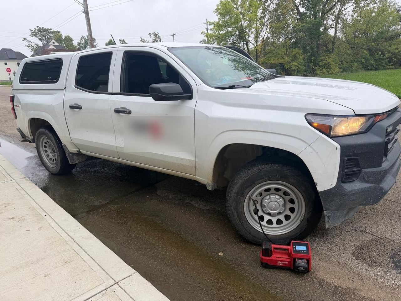 Portable tire inflator connected to the front tire of a white pickup truck parked at a curb