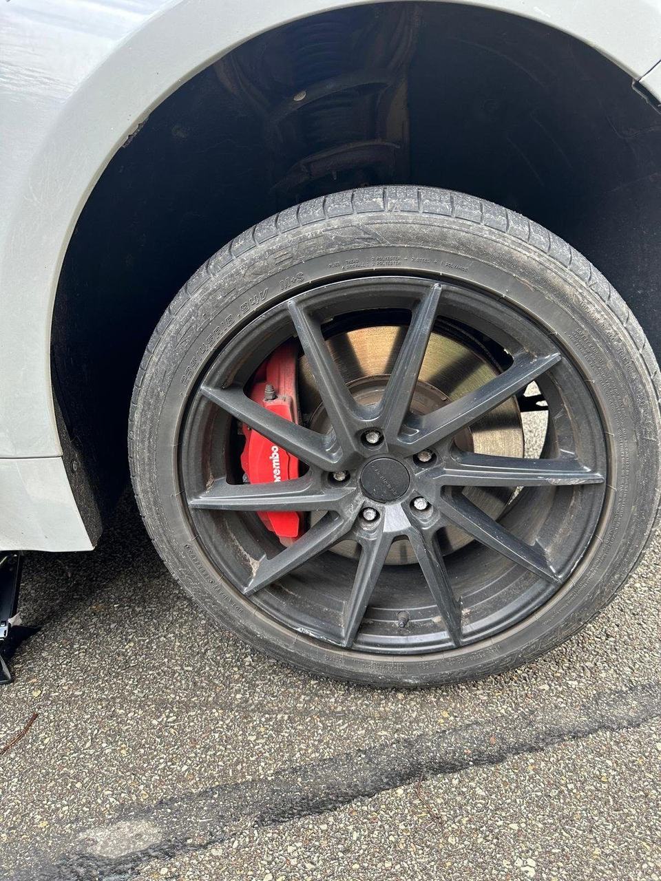 Red brake caliper and rotor seen through a black alloy wheel, with the car raised on a jack