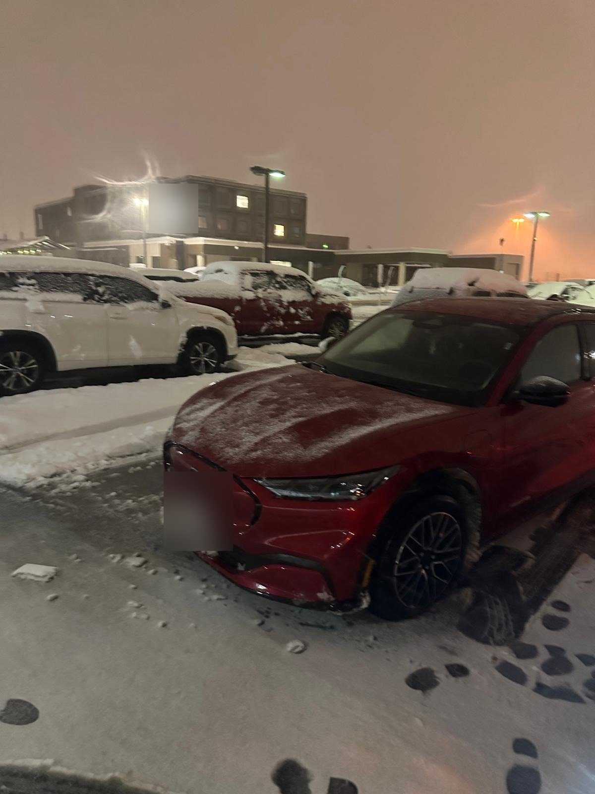 Red crossover in a snowy parking lot at night, with snow-covered cars behind it