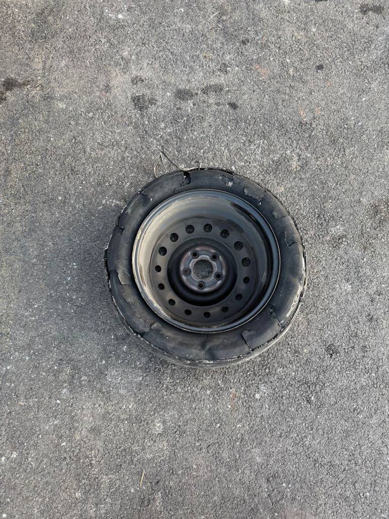 Shredded tire on a black steel wheel lying on asphalt after it came off the car