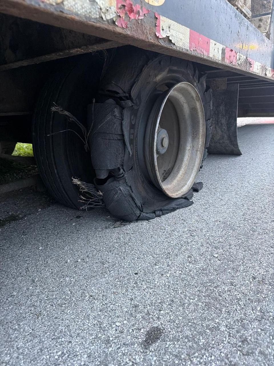 Trailer tire torn apart down to the steel rim, with loose cords hanging out, on an asphalt lot