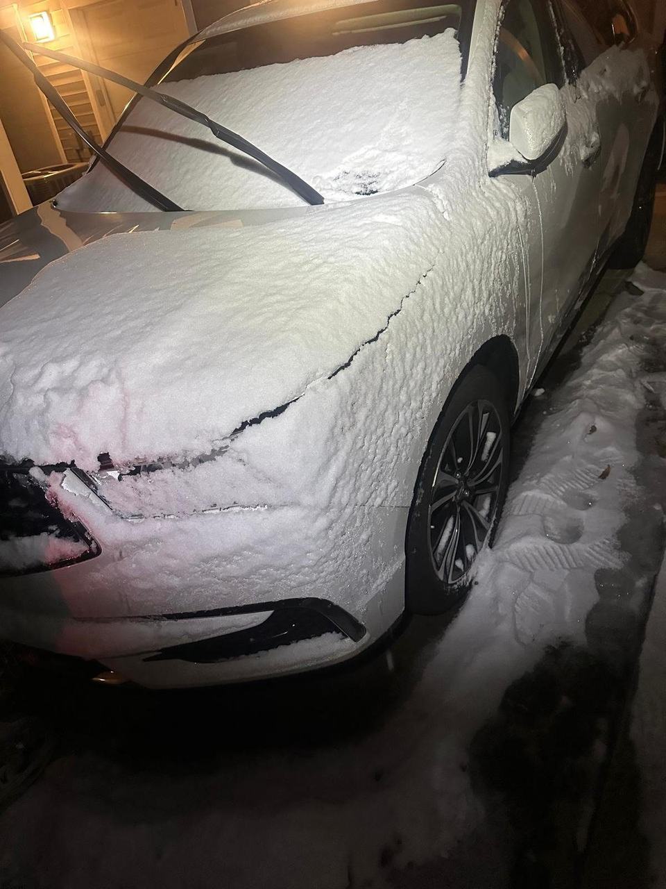 White SUV covered in snow at night, with the windshield wipers lifted off the glass