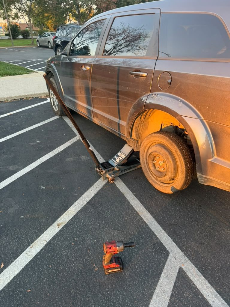 Grey SUV in a parking lot on a floor jack with a spare wheel fitted and an impact wrench on the ground