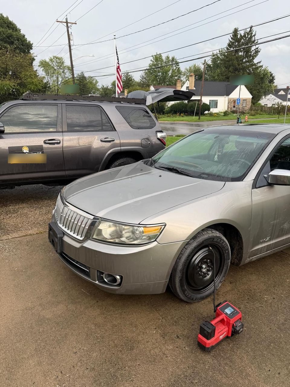 Silver sedan with a black steel spare wheel fitted on the front, a portable tire inflator connected, and the Roadmate service truck parked behind