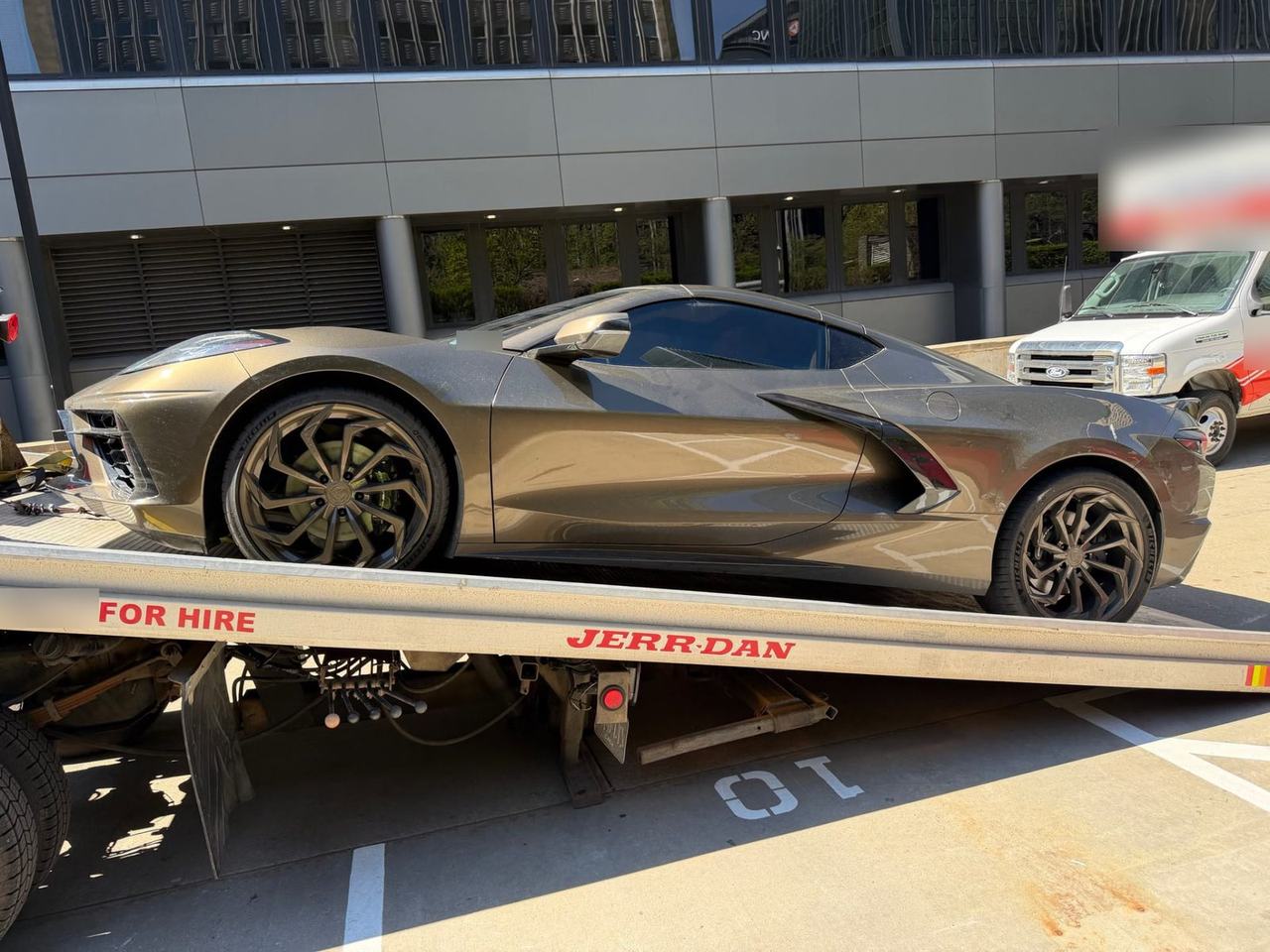 Low sports car strapped down on the tilted bed of a flatbed tow truck in a parking area