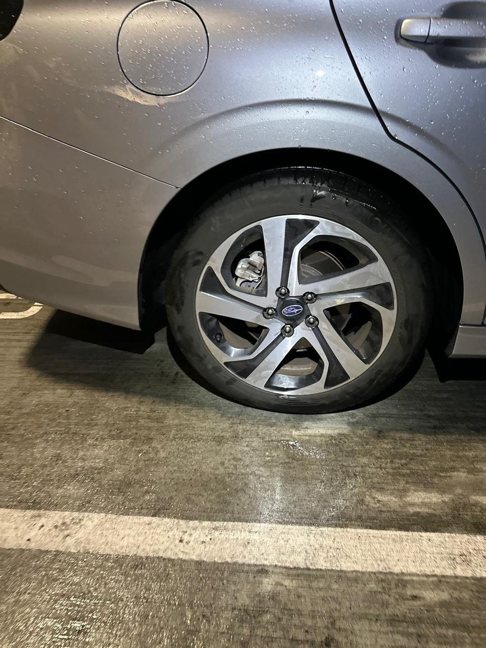 Gray Subaru sedan with a low rear tire parked in a parking garage