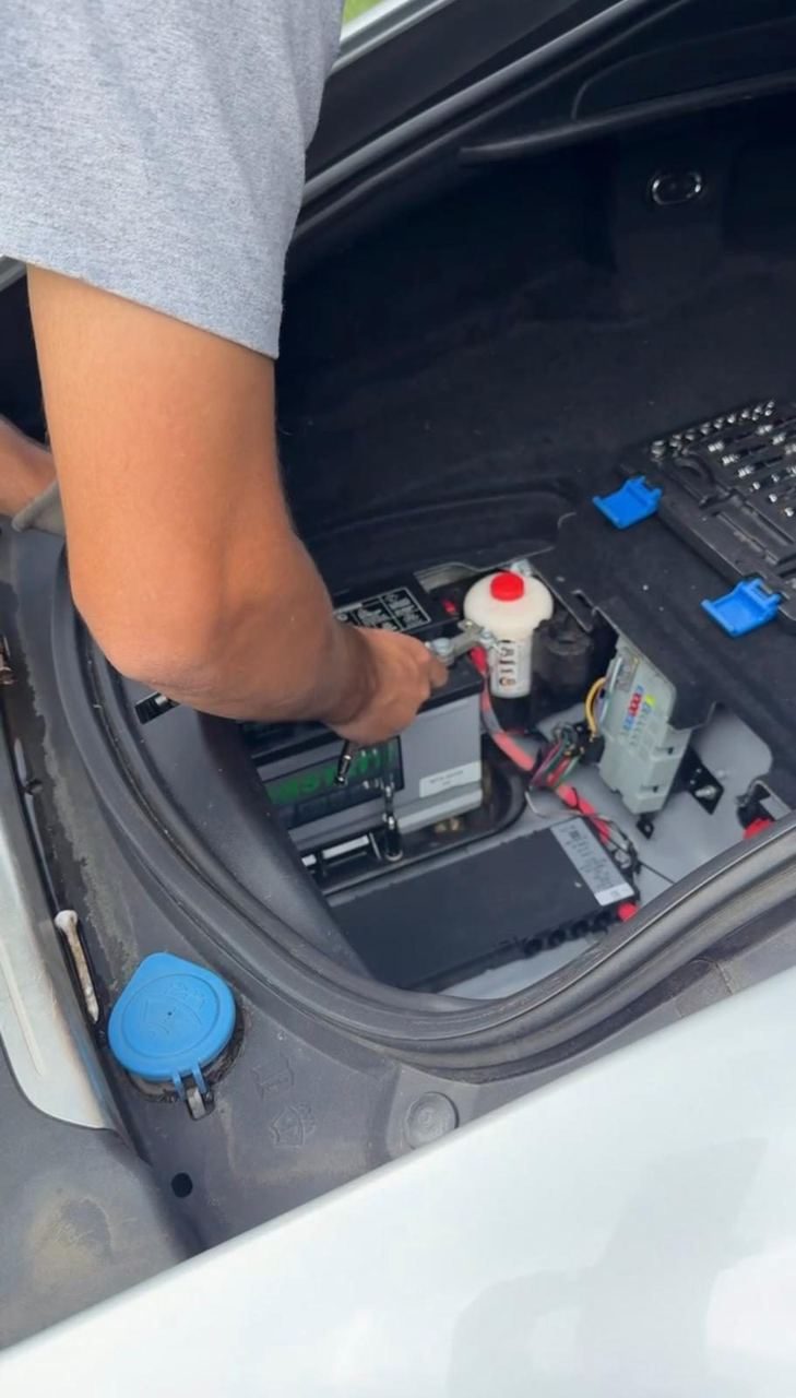 Technician tightening a terminal on a battery mounted in a car's trunk