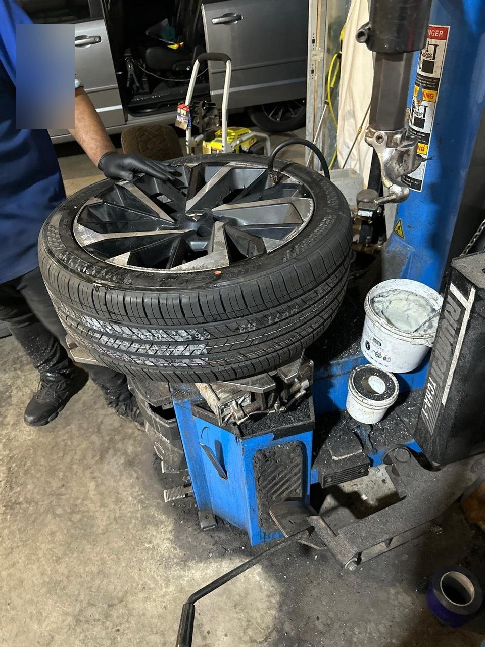 Gloved hand on a wheel and tire mounted on a tire changer in a shop