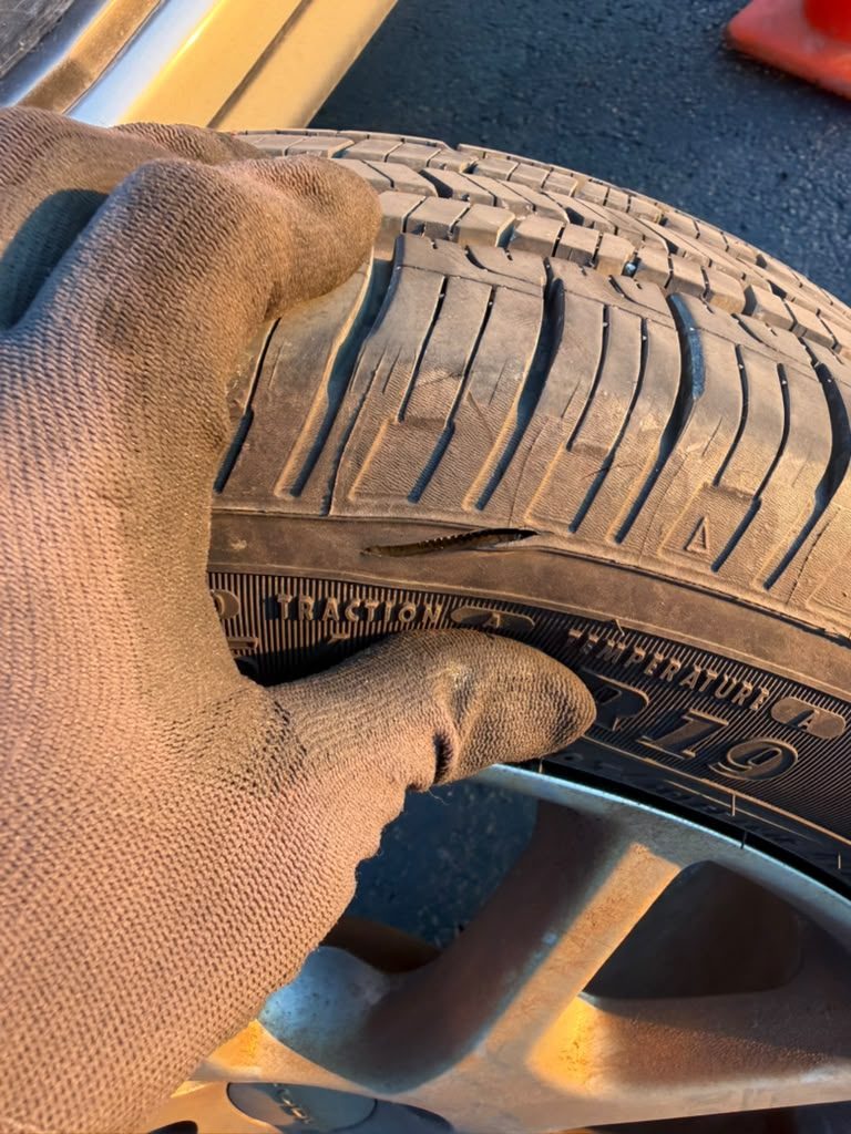 Gloved hand pointing to a cut where the tire tread meets the sidewall, damage that cannot be plugged