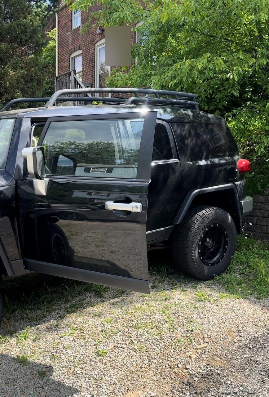 Black Toyota FJ Cruiser parked on a gravel driveway with its front door open