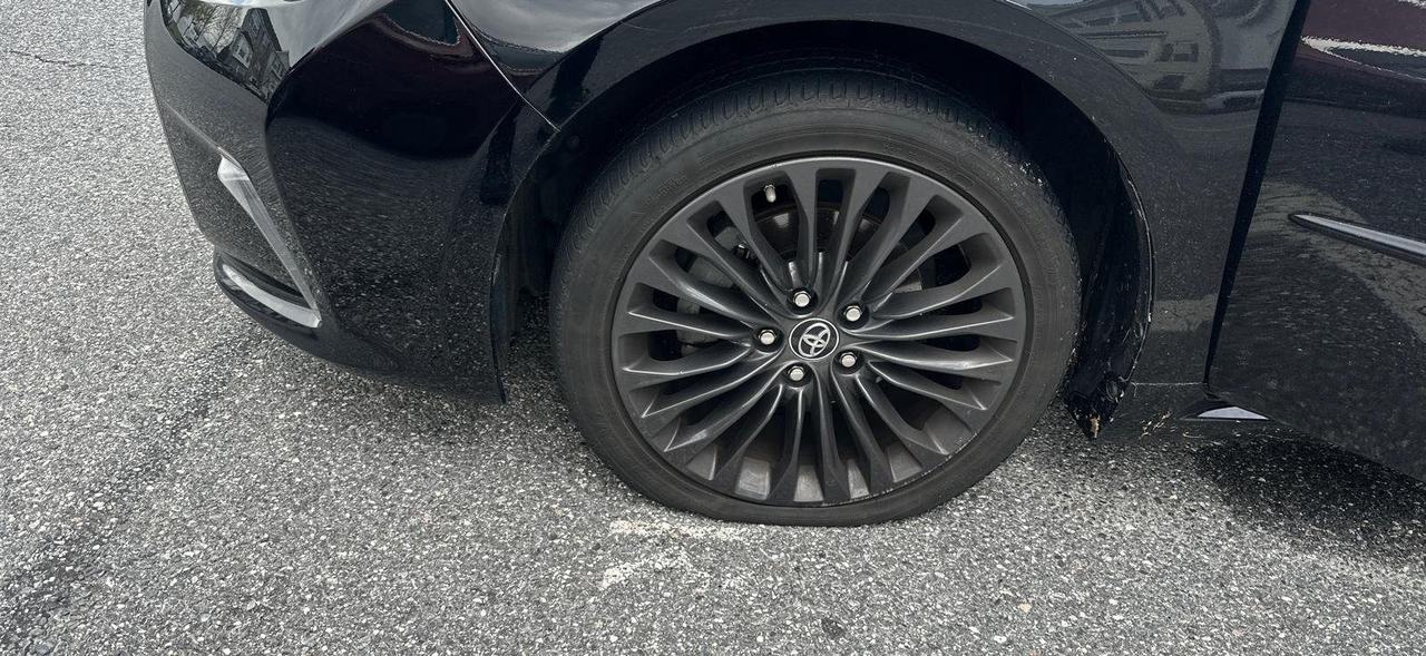 Black Toyota with a flat front tire, the valve stem visible near the top of the rim